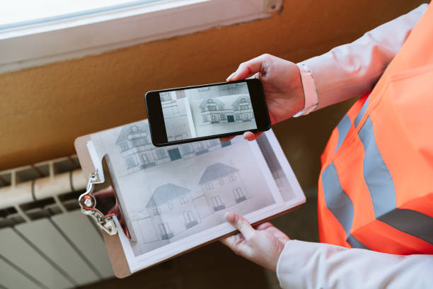 unrecognizable architect woman in construction site using mobile phone holding blueprints stock photo