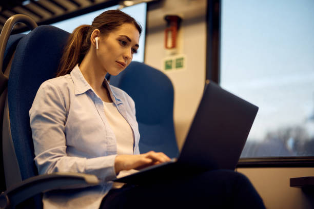 istock Young woman with earbuds using laptop during her train journey. 1389549054