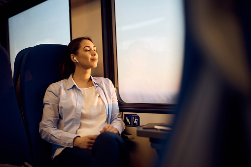 Young woman sitting by the window with her eyes closed while traveling by train. Copy space.
