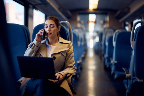 Young businesswoman using laptop and talking on the phone while commuting to work by train.