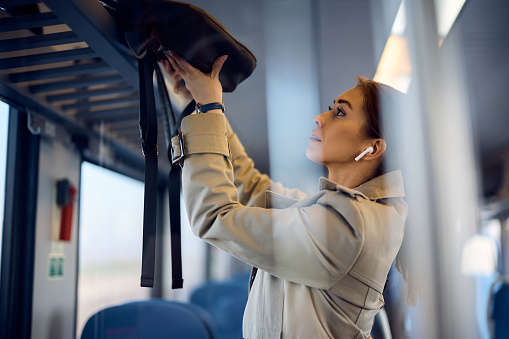 Young woman putting her bag on luggage rack while commuting by train.