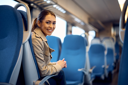 Young happy woman traveling by train and looking at camera.