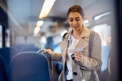 Young woman reading seat number on a ticket while traveling by train. Copy space.