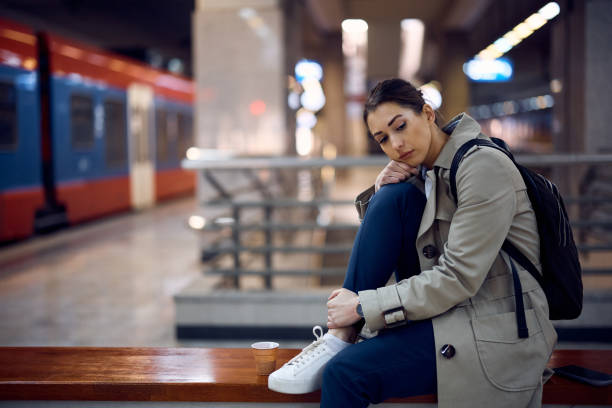 Young feeling sad while waiting for someone and sitting alone on a bench at train station.