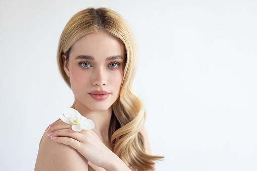 Close up studio shot of a beautiful blonde woman, holding orchid flower.