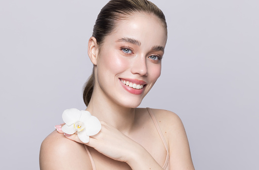 Close up studio shot of a beautiful blonde woman, holding orchid flower.