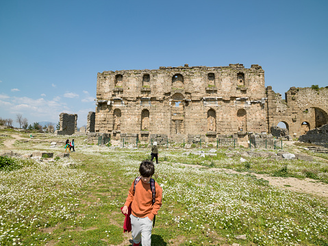 Photo of 8,5 years old boy exploring ancient city of Aspendos during springtime. He is wearing an orange sweater. Shot under daylight.
