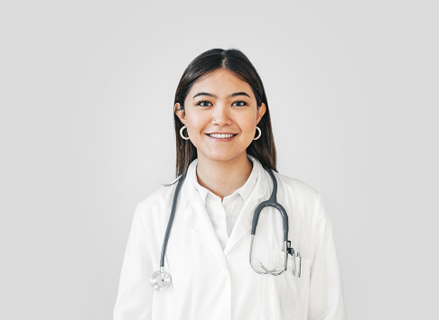 Portrait of a smiling female doctor standing and smiling against white wall. Woman healthcare worker wearing lab coat with stethoscope on her neck.