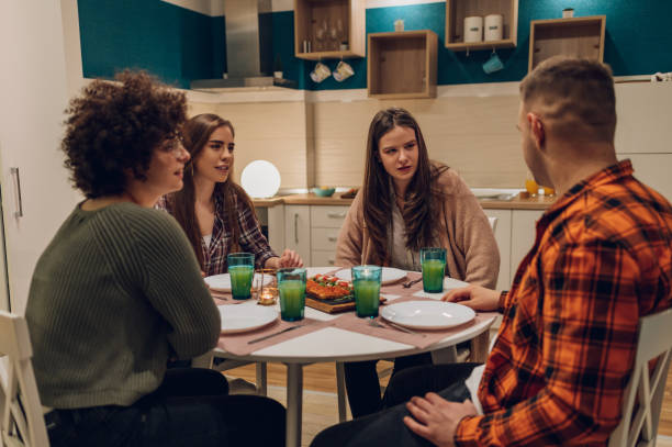 istock Group of friends enjoying dinner while sitting at the kitchen table together 1389557496
