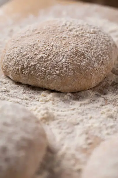 Balls of Italian ciabatta bread or pizza dough rising on floured bakers wood work surface.