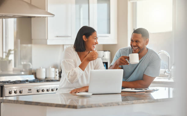 shot of a couple drinking coffee while using a laptop in the kitchen at home - coffee cafe drinking couple imagens e fotografias de stock