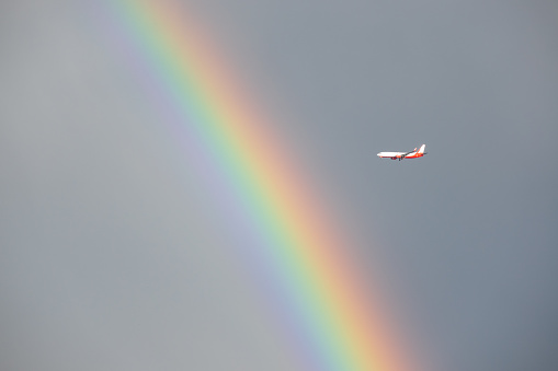 Airplane flying through rainbow on the sky. No people are seen in frame.