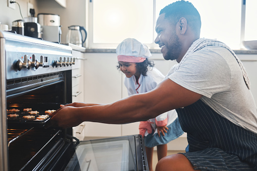 Foto de un hombre y su hija poniendo una bandeja para hornear en el horno photo