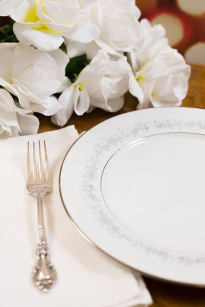 istock Place setting on table with bouquet of white roses. 1389560221