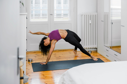 Fit yogi woman working out in fitness mat. Healthy woman in sportswear doing yoga bridge position in bedroom.