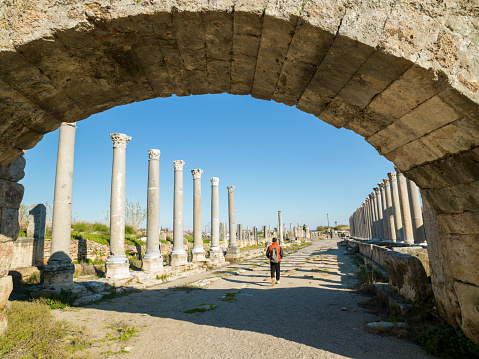 Photo of adult man visiting ancient city of Perge, Antalya, Turkey. He is wearing a red colored coat. Shot under daylight.
