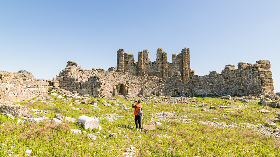 Photo of adult man traveling in ancient city of Aspendos. He is wearing a red coat. Shot under daylight during springtime.