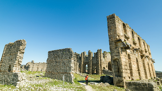 Photo of adult man traveling in ancient city of Aspendos. He is wearing a red coat. Shot under daylight during springtime.