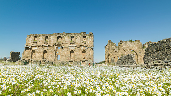 Photo of adult man traveling in ancient city of Aspendos. He is wearing a red coat. Shot under daylight during springtime.