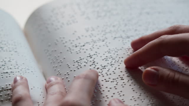 Blindman reading braille book using his fingers, poorly seeing person learning to read, disabled people. Close-up of touching letters on sheet of paper