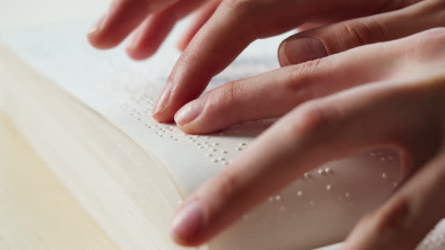 Blindman reading braille book using his fingers, poorly seeing person learning to read, disabled people. Close-up of touching letters on sheet of paper