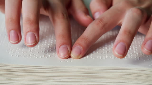 Blind person reading with his hands using braille book, poorly seeing man learning to read, disabled people. Close-up of touching letters on sheet of paper