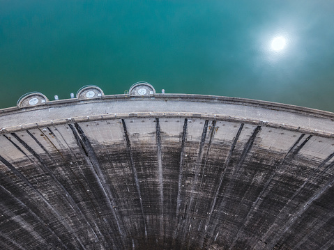 Aerial view  of a dam wall and sun reflecting in the water of the dam. Hydroelectric power plant.