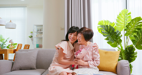 asian daughter give surprise flowers to her mom and celebrate happy mothers day in living room at home