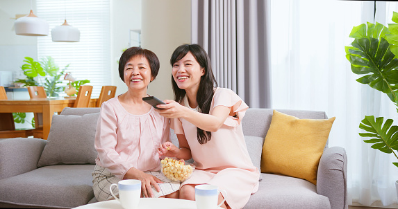 asian mother and daughter are watching tv and chat together in living room at home