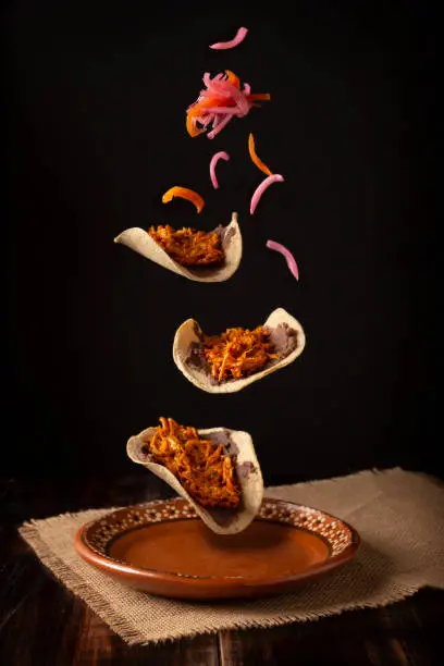 Creative food image of Mexican Tacos de Cochinita Pibil and onion with habanero chili falling on traditional mexican clay dish. Levitation photography.