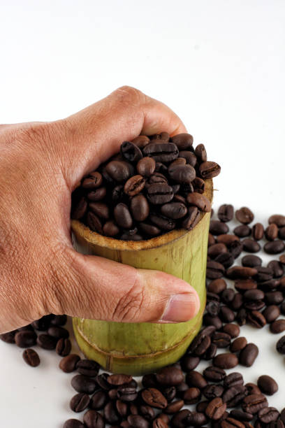 The hand is picking up a bamboo mug with coffee beans and coffee beans scattered on the white background.