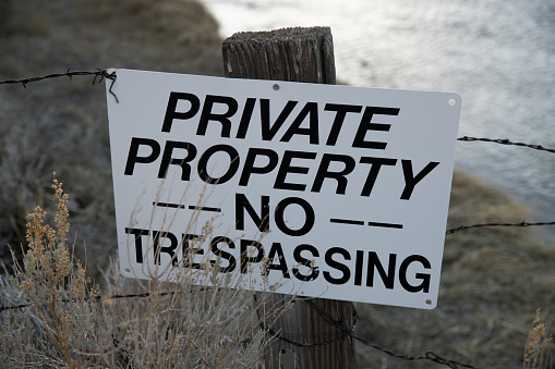 Close up of a private property sign on a post with barbed wire fencing