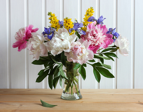 summer composition with a bouquet of garden flowers, peonies and irises in a glass vase.