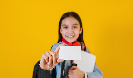 Young latin teen child girl student holding a blank empty card isolated on yellow background in Latin America