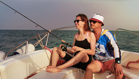 A man 45-46 years old and a woman 30-35 years old on an evening fishing in the sea on a speedboat. A man hugs a woman. The woman smiles.