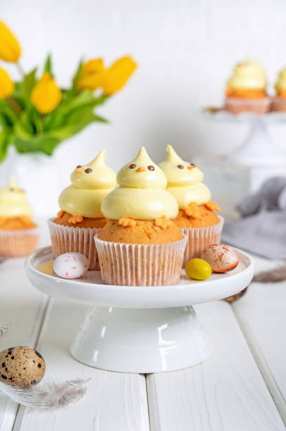 istock Cute Easter chick cupcakes. Vanilla cupcakes with buttercream on a white stand with fresh flowers on a white wooden background. Copy space. 1389621157