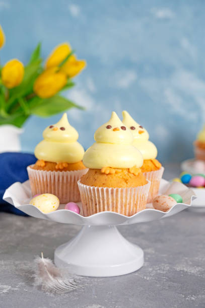 istock Cute Easter chick cupcakes. Vanilla cupcakes with buttercream on a white stand with fresh flowers on a white wooden background. Copy space. 1389621163