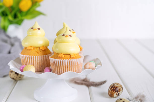 istock Cute Easter chick cupcakes. Vanilla cupcakes with buttercream on a white stand with fresh flowers on a white wooden background. Copy space. 1389621164