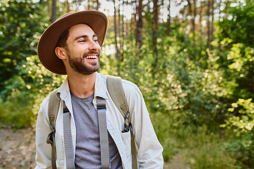 Laughing young man hiking in forest during summer trekking