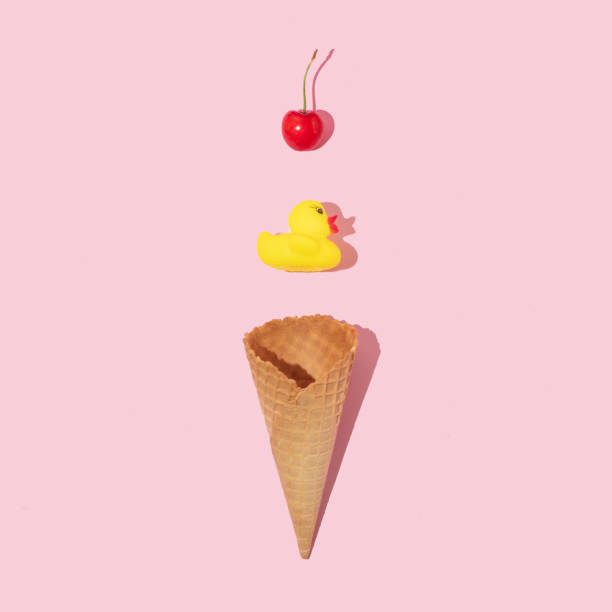 istock Creative composition with ice cream cone, yellow rubber duck and bright red cherry on pastel pink background. Summer dessert art direction. Summer food minimal concept. 1389627632