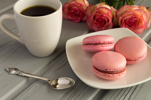 Pink macaroons and coffee on the gray wooden background. Close-up.
