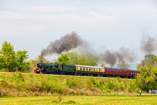 Hereford, UK - April 22, 2019: UK steam train on an express nostalgic tour passing through Herefordshire. People are pictured on the train and watching from a field below