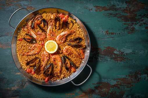 Seafood Paella Mediterranean diet recipe with shrimp, squid and mussels on rustic green wooden background