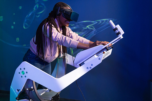 African-American young woman playing VR video game. She wears VR goggles, using game controllers