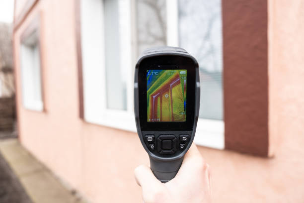 una mano masculina sostiene una cámara termográfica en la ventana de una casa. búsqueda de pérdida de calor en casas particulares - heat leak fotografías e imágenes de stock