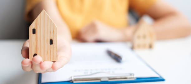istock Woman holding home model during signing home contract documents. Contract agreement, real estate,  buy and sale and insurance concepts 1389632652