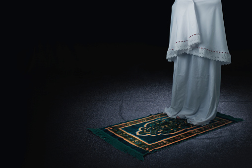 Muslim woman in veil in praying position (salat) on the prayer rug