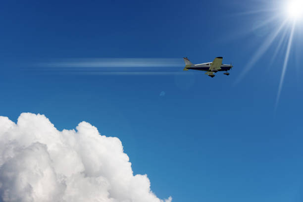 pequeño avión en movimiento contra un cielo azul claro con nubes y rayos de sol - avión ultraligero fotografías e imágenes de stock