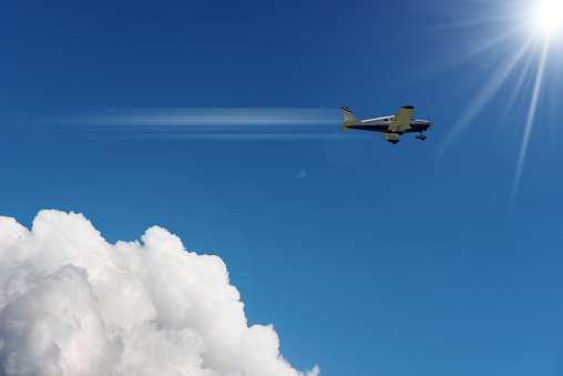 Small Airplane in Motion against a Clear Blue Sky with Clouds and Sunbeams