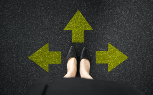 Choice and business concept. Selfie of feet and legs shoes black on road floor. Top view of businesswoman standing with many direction arrow choices, left, right or move forward. Taking decisions. elección y concepto de negocio. selfie de pies y piernas zapatos negros en el suelo de la carretera. vista superior de la mujer de negocios de pie con muchas opciones de flecha de dirección, izquierda, derecha o avanzar. toma de decisiones.